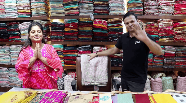 Poonam Ji showcasing Royal Red Bridal Lehenga shopping at JMS Studio Store with colorful fabrics in the background
