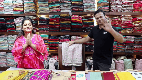 Poonam Ji showcasing Royal Red Bridal Lehenga shopping at JMS Studio Store with colorful fabrics in the background