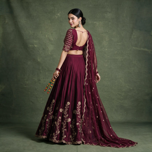 Back view of the wine lehenga choli with open-back blouse, gold floral embroidery on the skirt and the dupatta trailing behind