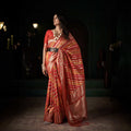 Orange silk saree with gold zari stripes and ornate woven border, draped