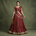 Model in a maroon pure Chanderi chaniya choli with gold zari-weave lace on the hem, blouse sleeves and dupatta, holding dandiya sticks