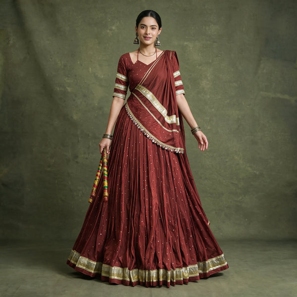 Model in a maroon pure Chanderi chaniya choli with gold zari-weave lace on the hem, blouse sleeves and dupatta, holding dandiya sticks