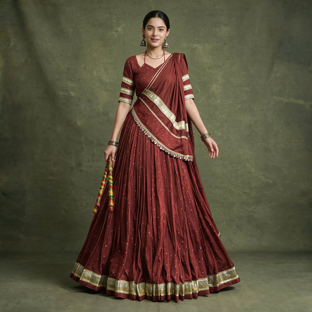 Model in a maroon pure Chanderi chaniya choli with gold zari-weave lace on the hem, blouse sleeves and dupatta, holding dandiya sticks