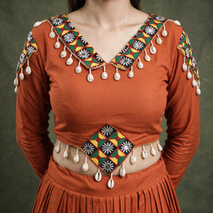 Close-up of the orange blouse with a patchwork neckline and cowrie shells hanging from the neckline and waist