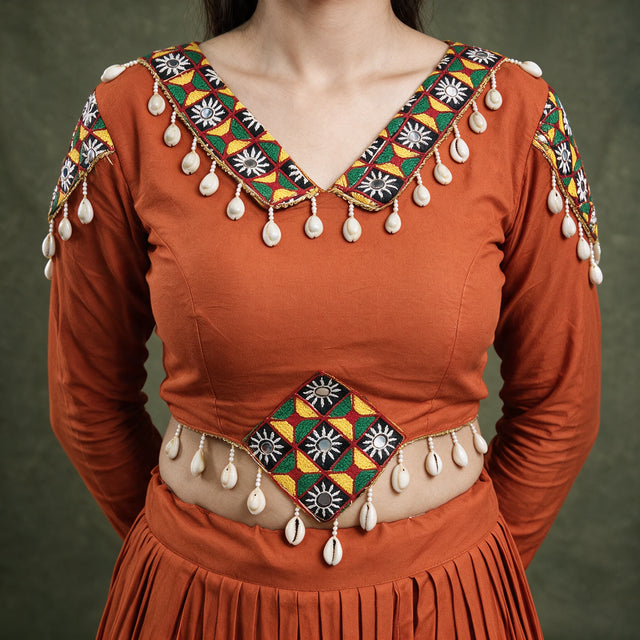 Close-up of the orange blouse with a patchwork neckline and cowrie shells hanging from the neckline and waist