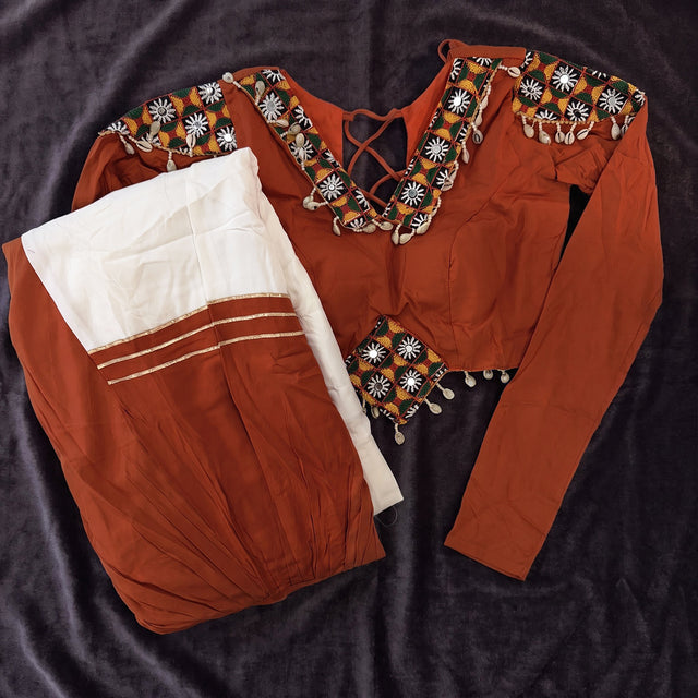 Flat lay of the orange full-sleeve blouse with cowrie and patchwork trim and the orange and white skirt