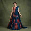 Model in a navy chaniya choli with red printed panels and cowrie shell trim, with a navy dupatta, holding dandiya sticks