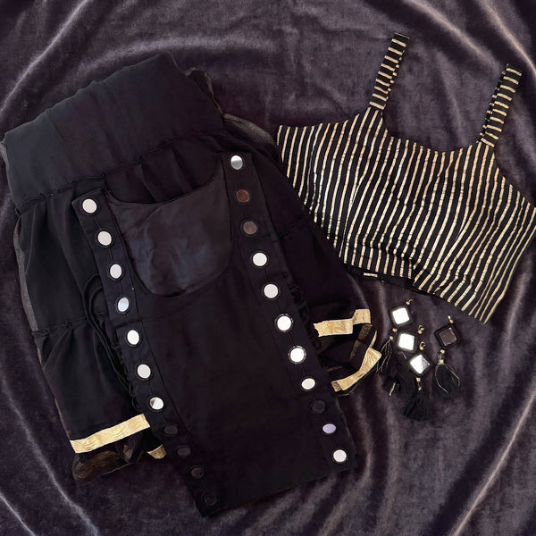 Flat lay of the black tiered skirt and koti with round silver discs, the black and gold striped blouse and tassels