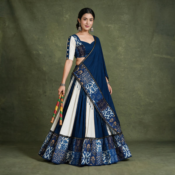 Model in a navy and white wedge-panelled chaniya choli with a printed indigo border and a navy dupatta with a mirror lace edge, holding dandiya sticks