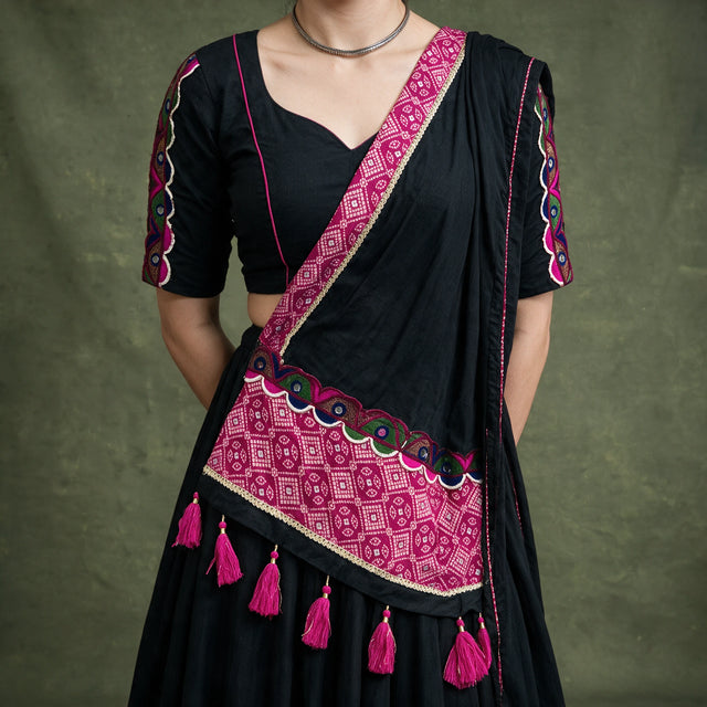 Close-up of the black blouse with embroidered sleeves and the black dupatta with a pink bandhej-print border and pink tassels
