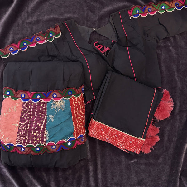 Flat lay of the black skirt with a multicolour patchwork border, the black blouse and the black dupatta with pink tassels