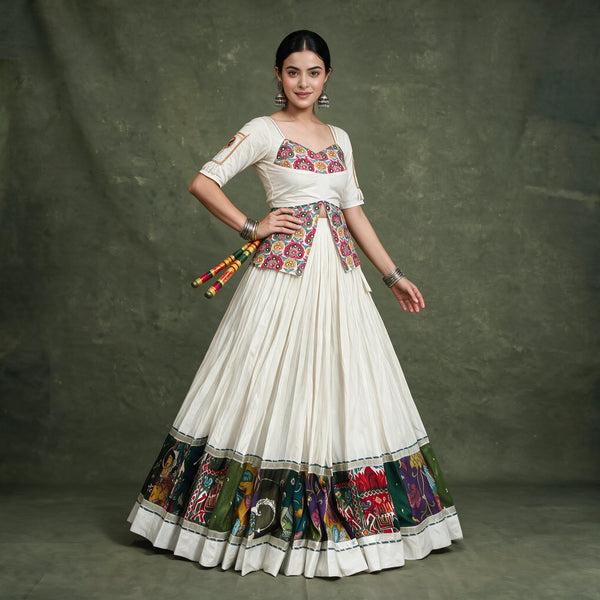 Model with a hand on her hip in the ivory chaniya choli, showing the long embroidered blouse and the multicolour hem border