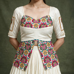 Close-up of the ivory blouse with a multicolour embroidered bodice and long embroidered peplum, with embroidered patches on the sleeves