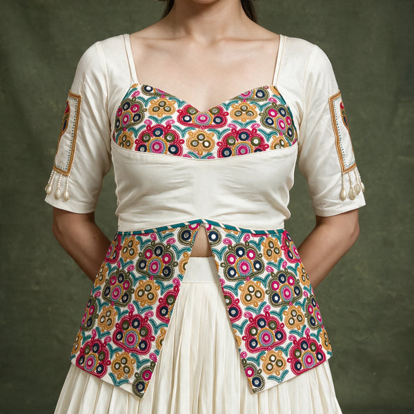 Close-up of the ivory blouse with a multicolour embroidered bodice and long embroidered peplum, with embroidered patches on the sleeves