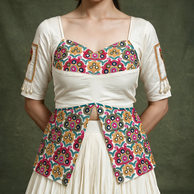 Close-up of the ivory blouse with a multicolour embroidered bodice and long embroidered peplum, with embroidered patches on the sleeves