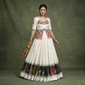 Model in an ivory khadi cotton chaniya choli with a long multicolour embroidered blouse and a multicolour panel border at the hem, holding dandiya sticks