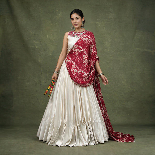 Model in an ivory monga silk chaniya choli with a maroon floral printed dupatta draped across the shoulder, holding dandiya sticks