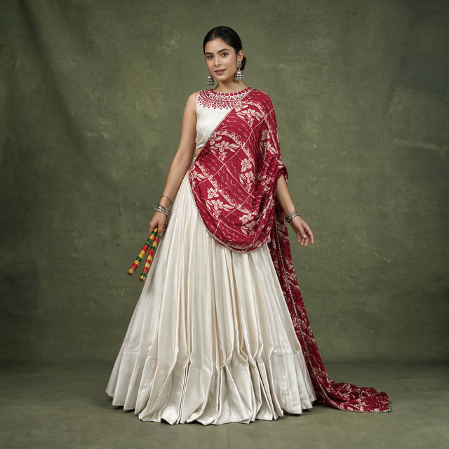 Model in an ivory monga silk chaniya choli with a maroon floral printed dupatta draped across the shoulder, holding dandiya sticks
