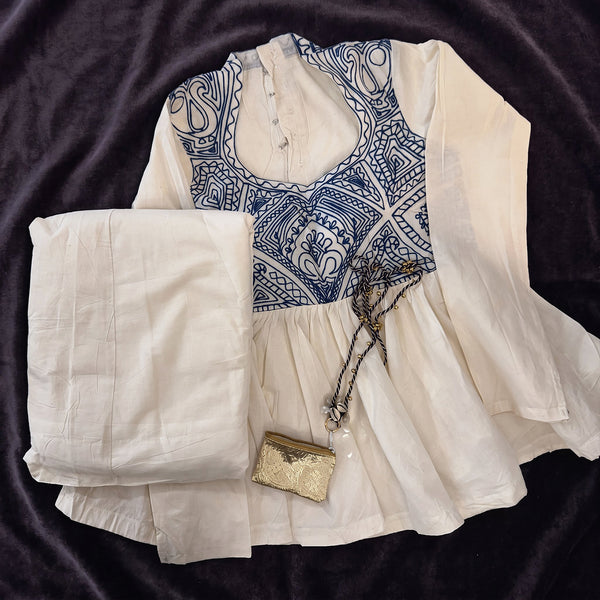 Flat lay of the ivory cotton top with a blue embroidered yoke, the ivory skirt and the small gold purse