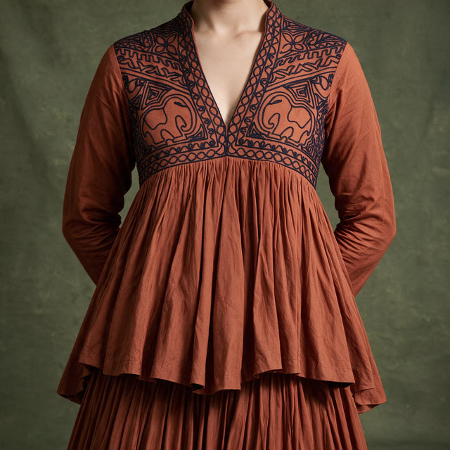 Close-up of the rust top with a dark embroidered V-neck yoke and gathered peplum