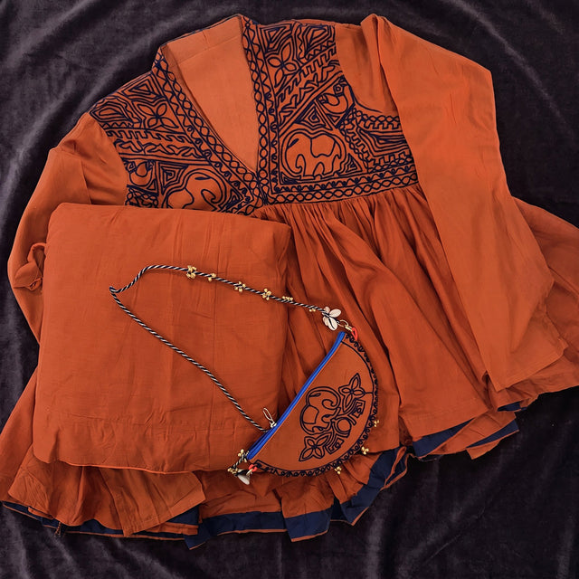 Flat lay of the rust top with a dark embroidered yoke, the rust skirt and the small embroidered purse