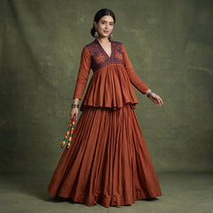 Model in a rust peplum top with a dark embroidered yoke over a full rust skirt, holding dandiya sticks