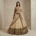 Beige embroidered lehenga with gold border, net dupatta, and tiered skirt on model