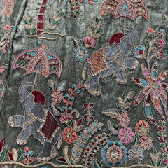 Close-up of olive lehenga fabric with colorful floral and bird-like threadwork embroidery