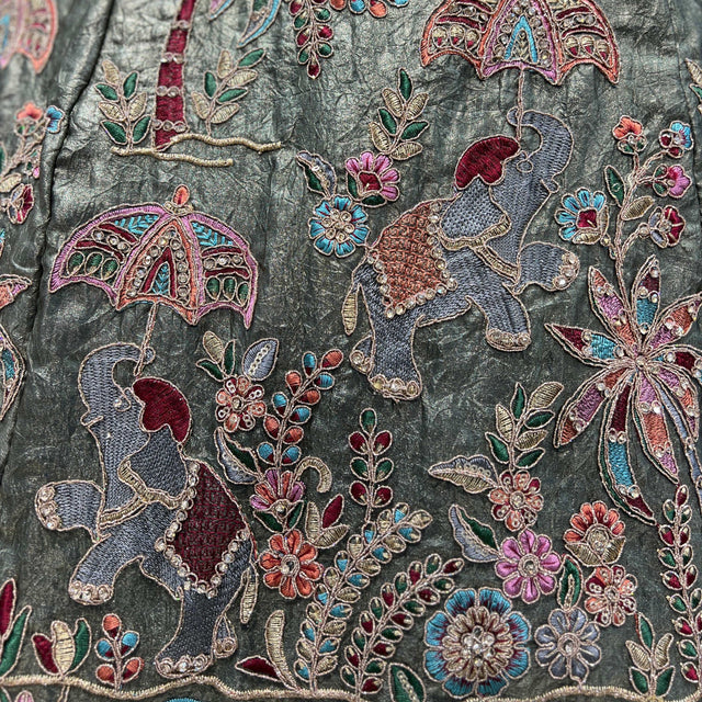 Close-up of olive lehenga fabric with colorful floral and bird-like threadwork embroidery