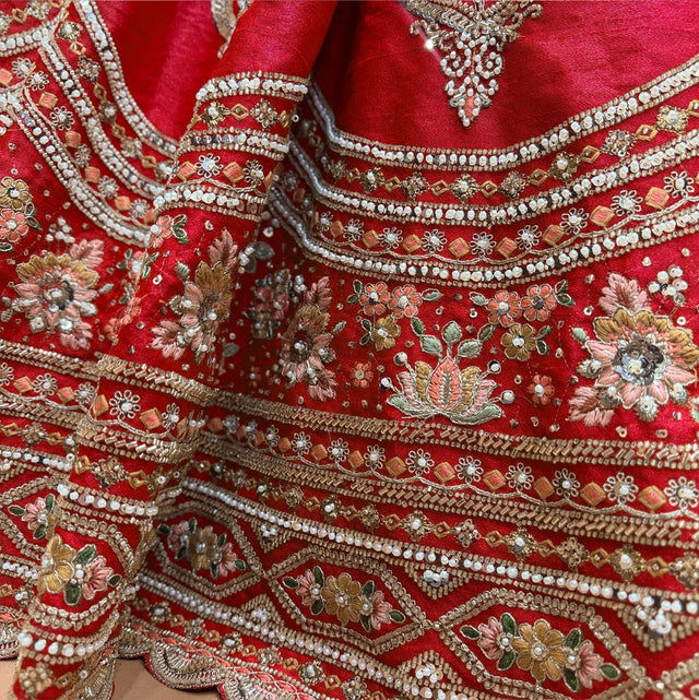 Close-up of red lehenga hem: pearl swags, zari bands and multicolour resham floral panel