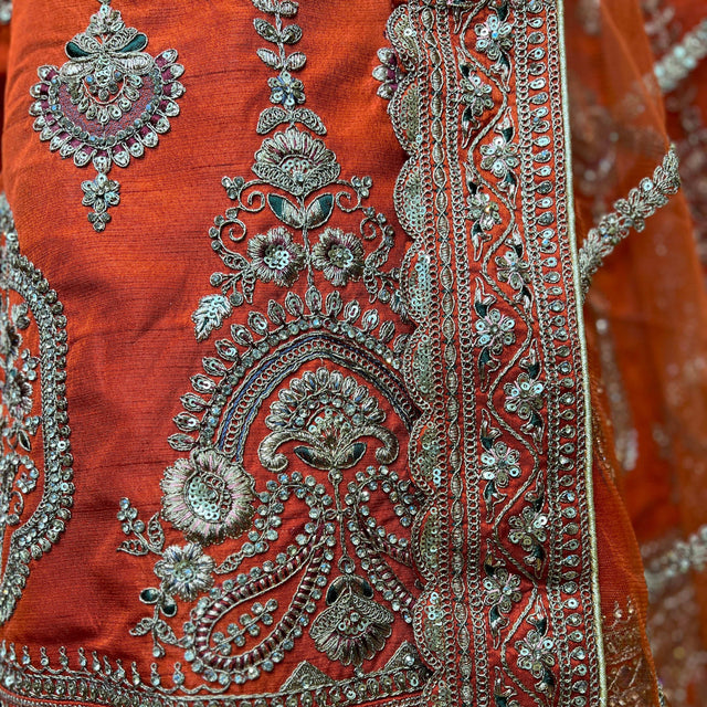 Close-up of rust orange lehenga fabric with detailed silver embroidery motifs
