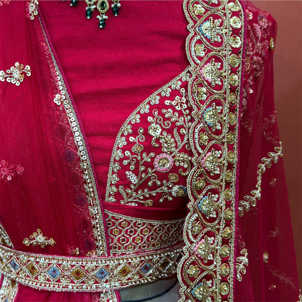 Raspberry lehenga blouse with V neckline, gold thread embroidery, and embellished trim