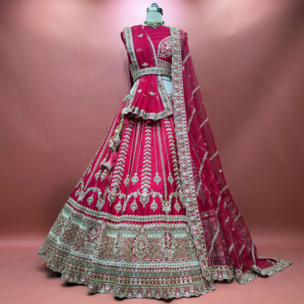 Raspberry bridal lehenga on mannequin with full tiered skirt and ornate border embroidery