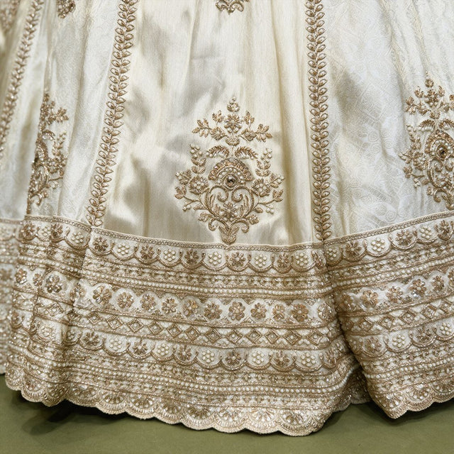 Ivory silk lehenga hem with gold leaf-vine columns, floral butis and stacked pearl and gold embroidered border