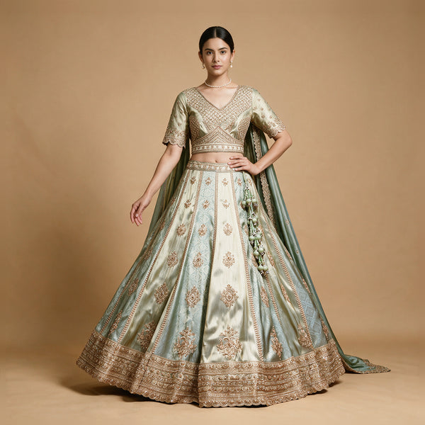 Model in a pista green and cream silk lehenga with gold embroidered motifs on alternating panels, embroidered blouse and green draped dupatta