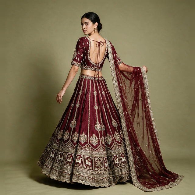 Back of a maroon raw silk blouse with scoop back and tie-up cords, gold embroidered skirt and net dupatta with scalloped border