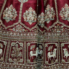 Close-up of maroon raw silk lehenga hem with white moti cow motifs in arched niches, gold floral panels and zari bands