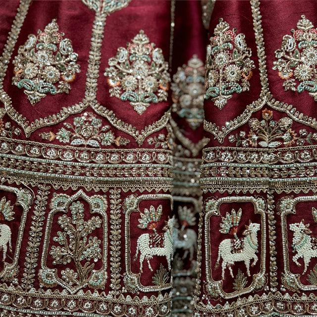 Close-up of maroon raw silk lehenga hem with white moti cow motifs in arched niches, gold floral panels and zari bands