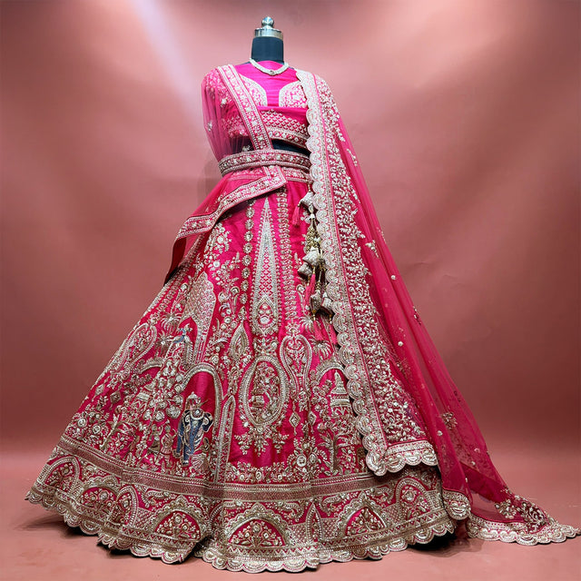 Rani pink raw silk bridal lehenga with elephant and rider procession embroidery, net dupatta and kamar belt
