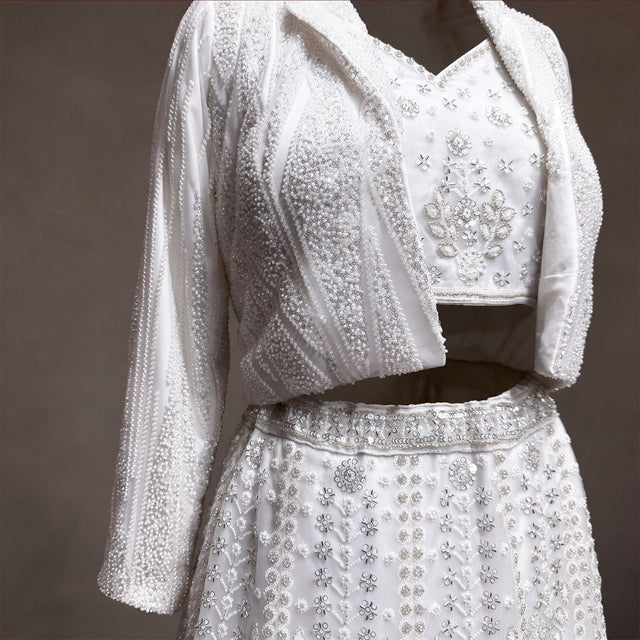 Close-up of pearl and sequin striped beaded jacket, handwork blouse and beaded waistband on white lehenga
