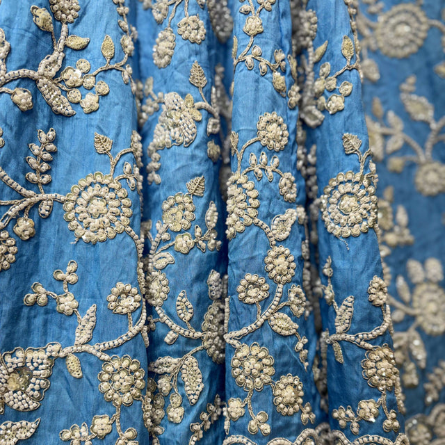 Close-up of blue fabric with dense gold floral and vine embroidery pattern