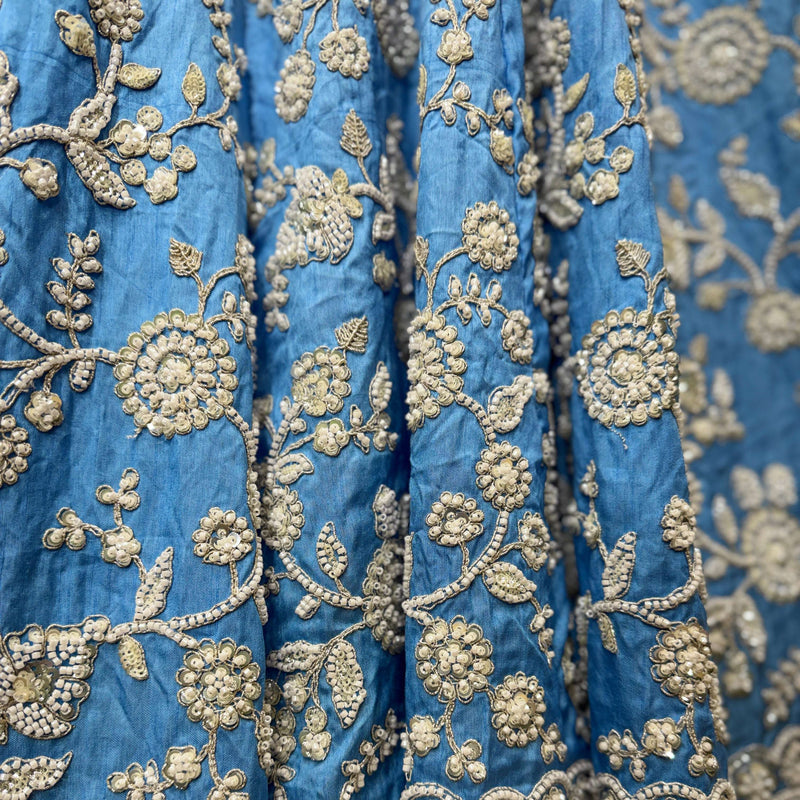 Close-up of blue fabric with dense gold floral and vine embroidery pattern