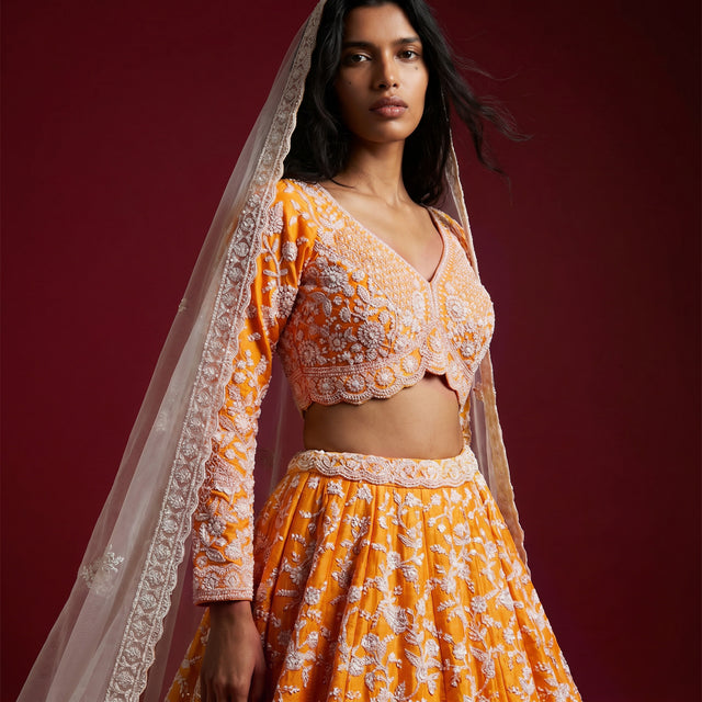 Orange lehenga and matching long-sleeve blouse with sheer dupatta, side view