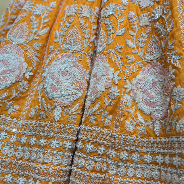 Close-up of orange lehenga fabric with silver bead and floral embroidery details