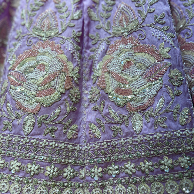 Purple fabric close-up with detailed beaded floral embroidery and decorative trim