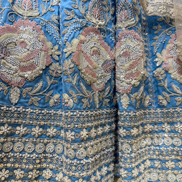 Close-up of blue lehenga fabric with dense beaded floral embroidery and gold trim border