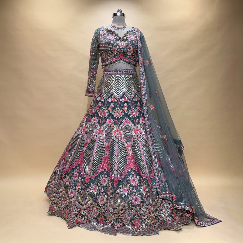 Embroidered lehenga on mannequin with floral motifs, gray-blue base, pink and silver trim