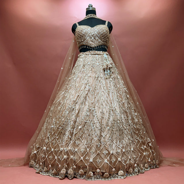 Champagne gold sequin and bead lehenga on a mannequin with sweetheart blouse, diamond lattice skirt, scalloped embellished hem and long net dupatta trailing behind