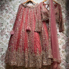 Dusty rose pink cutdana and pearl lehenga, full-sleeve blouse and pink net dupatta on hangers against floral wallpaper