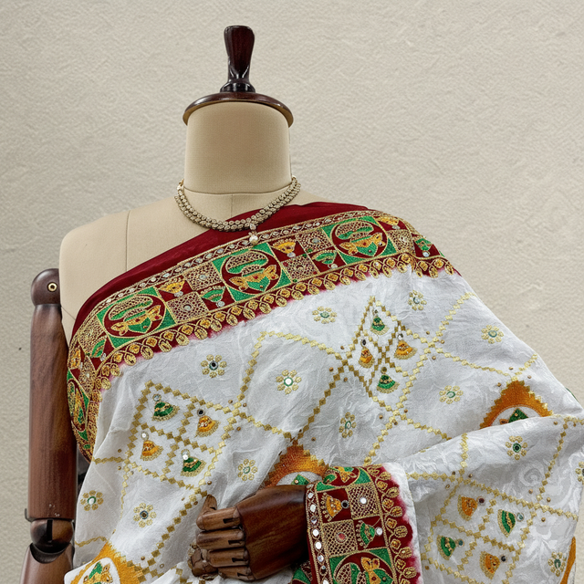 Close-up of white saree fabric with green, maroon and gold motif border over drape.